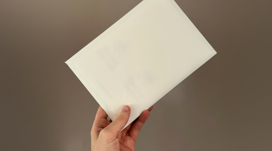 Hand holding a white square piece of paper against a brown background